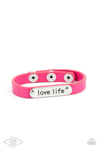 A silver plate engraved with the inspirational phrase “love life” is studded in place along a skinny strip of pink leather. Brushed in a shiny finish, the dainty band wraps around the wrist in a colorfully seasonal style. Features an adjustable snap closure.