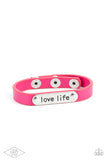 A silver plate engraved with the inspirational phrase “love life” is studded in place along a skinny strip of pink leather. Brushed in a shiny finish, the dainty band wraps around the wrist in a colorfully seasonal style. Features an adjustable snap closure.