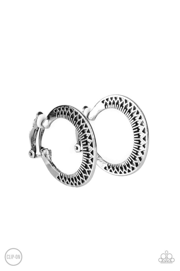 Stenciled in a petal-like texture, a silver frame delicately curves into a floral patterned hoop. Earring attaches to a standard clip-on fitting. Hoop measures approximately 1 1/2