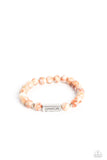 Meeting at the center of an elastic stretch bracelet, a silver, rectangular bar, hammered in a light sheen, is stamped with the word "peace" for a serene statement. Marbled, orange stone beads, and silver accents encircle the silver bar creating a calming, cheerful finish. As the stone elements in this piece are natural, some color variation is normal.